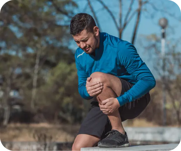 Man holding his knee in pain while outdoors, showing symptoms of an osteochondral (OCD) lesion and joint inflammation.