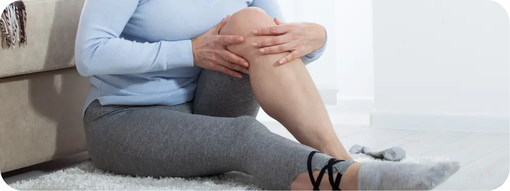 Woman sitting on the floor holding her knee due to inner knee pain and stiffness caused by medial compartment chondromalacia